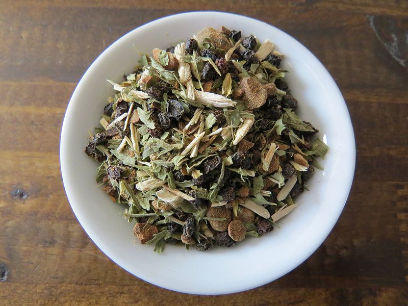 Top down shot of a small white bowl filled with a blend of bits of guarana, dried elderberries, eleuthro, and alfalfa.