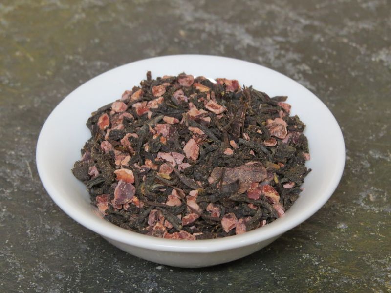 A small white bowl set on textured green stone, filled with a blend of ground cacao nibs and black tea.