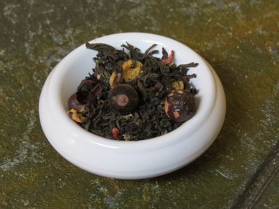 A small white bowl set on a textured stone table, filled with a blend of black tea and freeze dried black currants.
