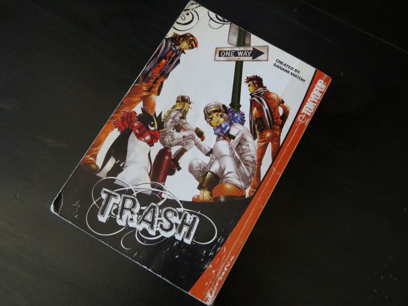 The cover of an anime with primary colours of black and red. It shows 4 humans in various poses, and a penguin in a scarf.