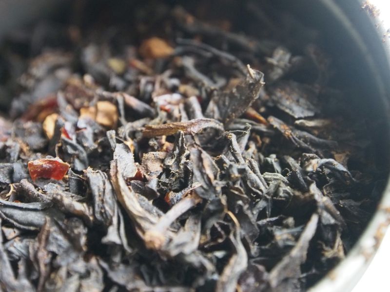 Closely zoomed in image of tea in a tin, the vanilla powder clinging to the tea leaves, rosehips and cinnamon blended in.