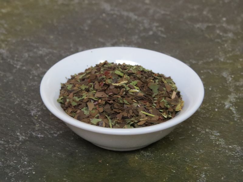 A small white bowl filled with a blend of roasted mate and peppermint sits on a textured green stone table.