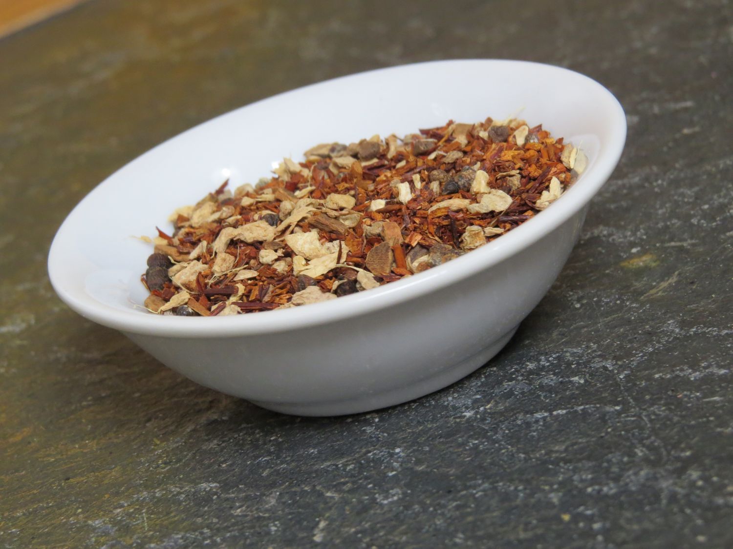 A small white bowl, canted at an angle, showing off a blend of red rooibos and chai spices.