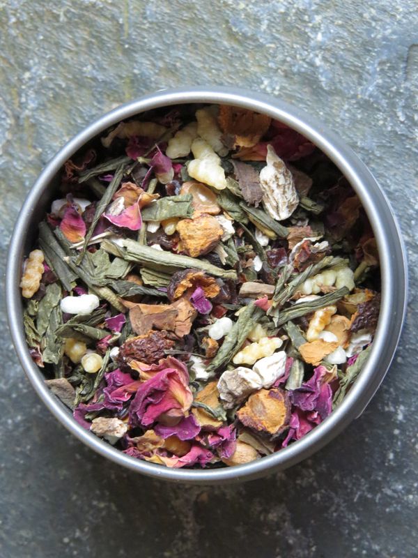 A small metal tin from above, full of a blend of green tea, genmai, rose petals, hawthorn berries, rosehips, and dandelion.