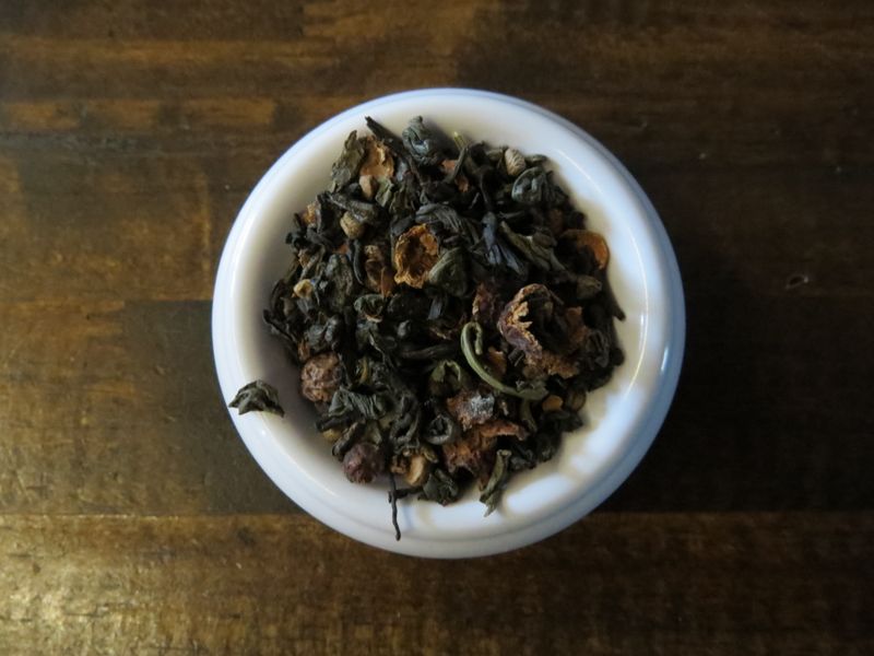 A small white bowl full of a blend of green tea, black tea, cardamom, and hawthorn berries.