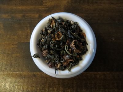 A small white bowl full of a blend of green tea, black tea, cardamom, and hawthorn berries.