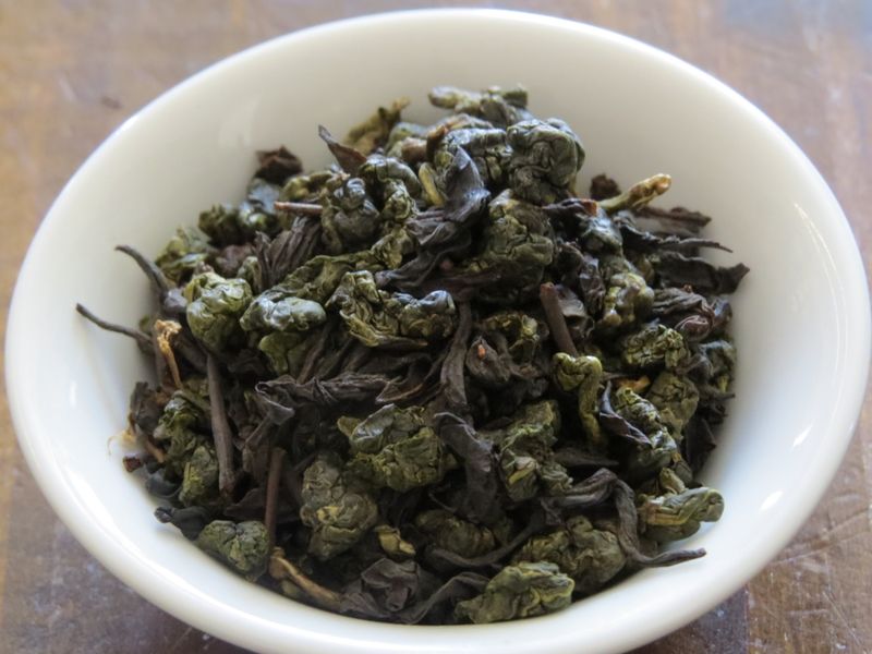Tightly rolled oolong blended together with black tea leaves, filling a small white bowl.