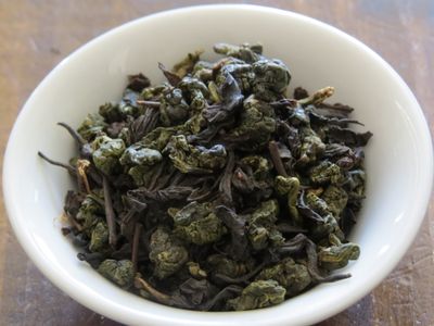 Tightly rolled oolong blended together with black tea leaves, filling a small white bowl.