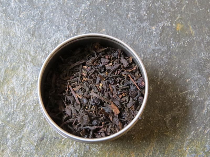 The image looks down into a small silver tin full of a blend of black teas, elderberries, and a light dusting of vanilla.