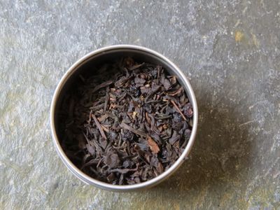 The image looks down into a small silver tin full of a blend of black teas, elderberries, and a light dusting of vanilla.
