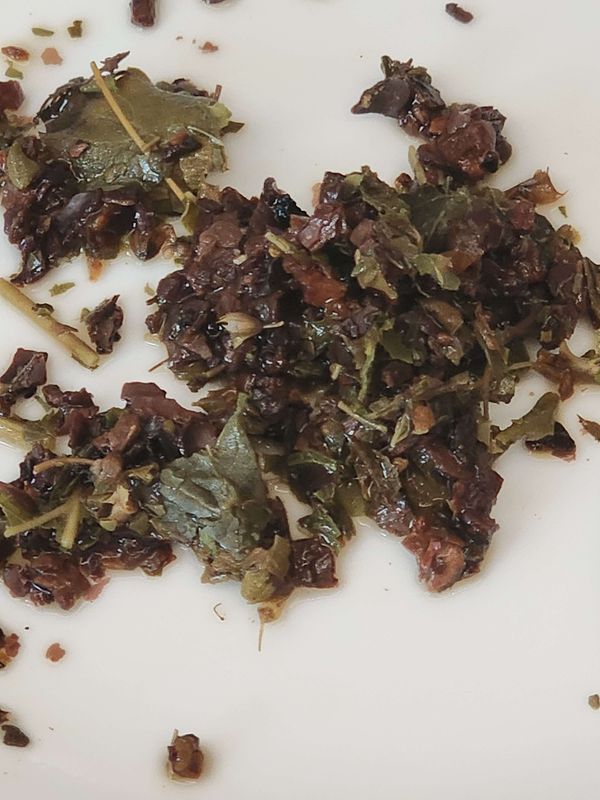 Wet tea tapped out onto a saucer, a mix of Tulsi and chicory and seaweed and cacao shells and blackberry leaf and cinnamon.