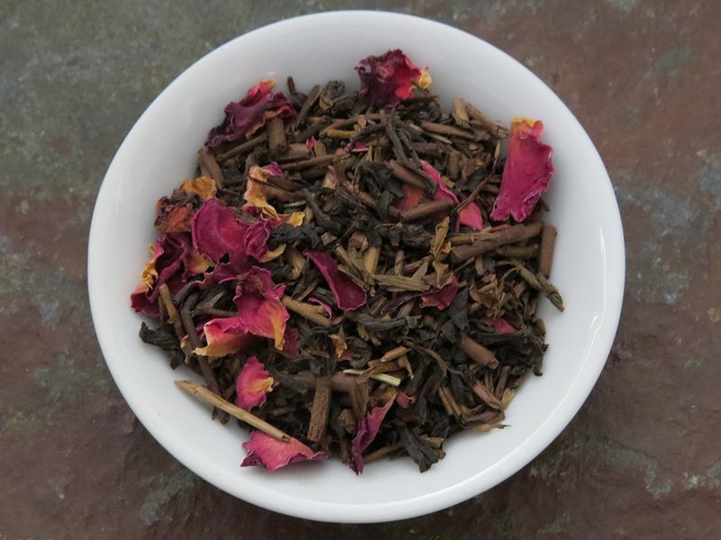 The image looks down into a small white bowl full of a blend of twig tea, black tea, rose petals, and rosemary.