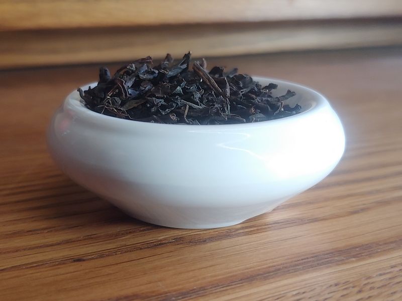 A small white bowl full of a blend of black teas, sitting on grained wood, with more of the same wood behind.