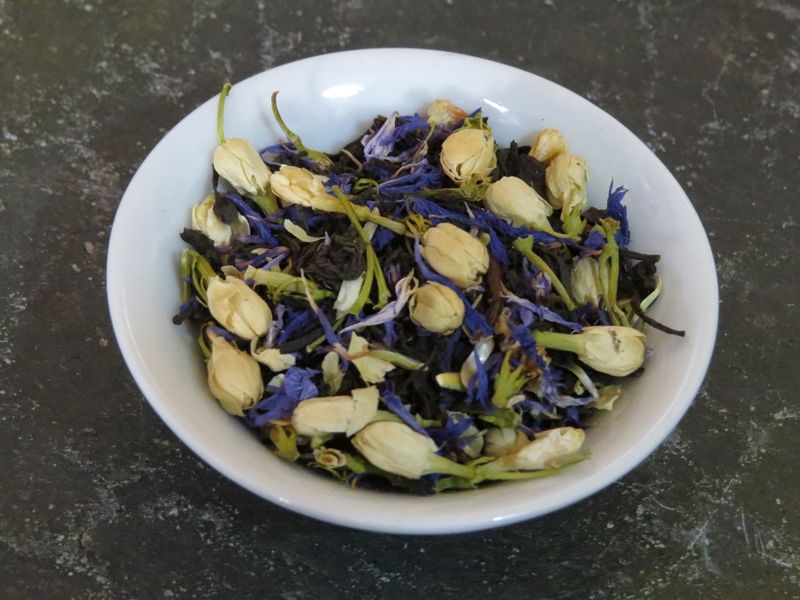 A small white bowl full of a blend of black tea, jasmine flowers, and cornflower petals. 