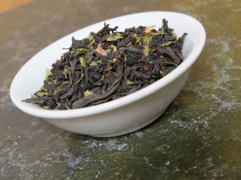 The image shows a white bowl full of a blend of black tea, elderberries, and peppermint.