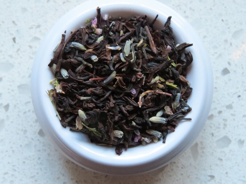 A small white bowl set of a speckled white counter, full of a blend of teas, lavender, and heather.