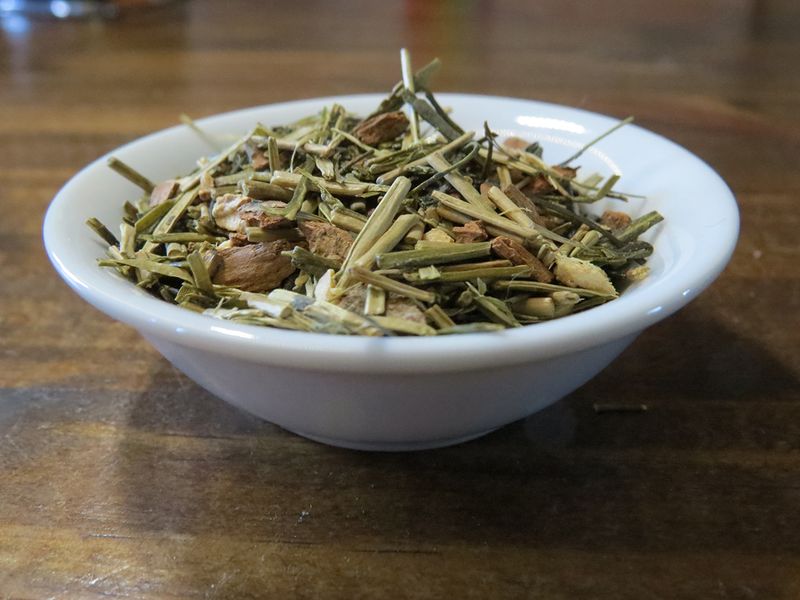 A small white bowl, seen at a slight angle, filled with a blend of green kukicha tea, cinnamon, cardamom, and ginger.