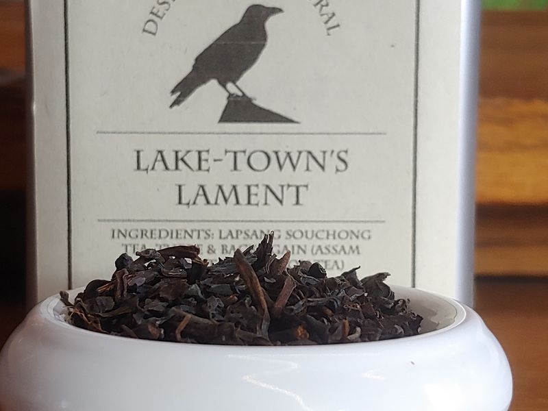 A blend of black teas in a small white bowl, set in front of a tin labeled "Lake'town's Lament."