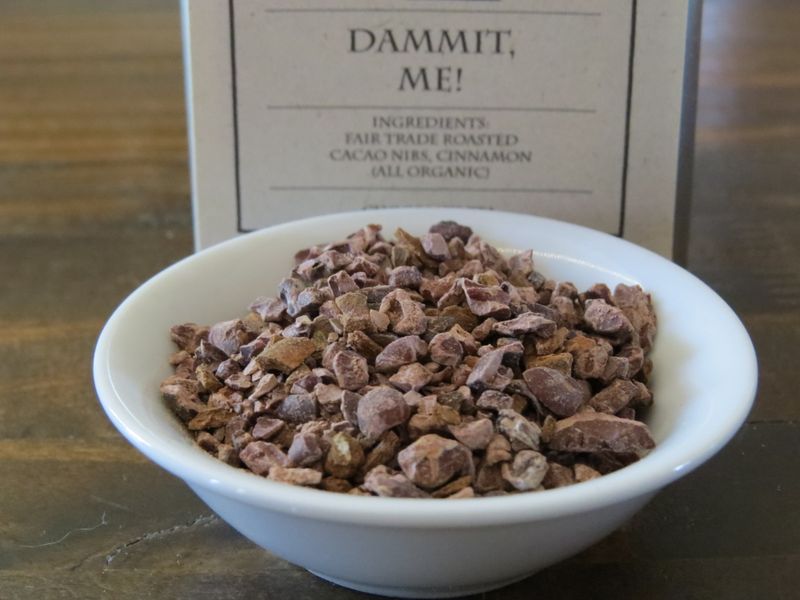 A small white bowl full of cacao nibs and cinnamon sits in front of a tin labeled "Dammit Me!"