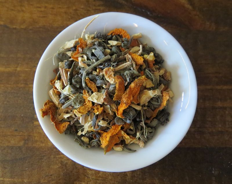 A small white bowl full of a blend of green tea, turmeric, lemon peel, Cinnamon, and Sarsaparilla.