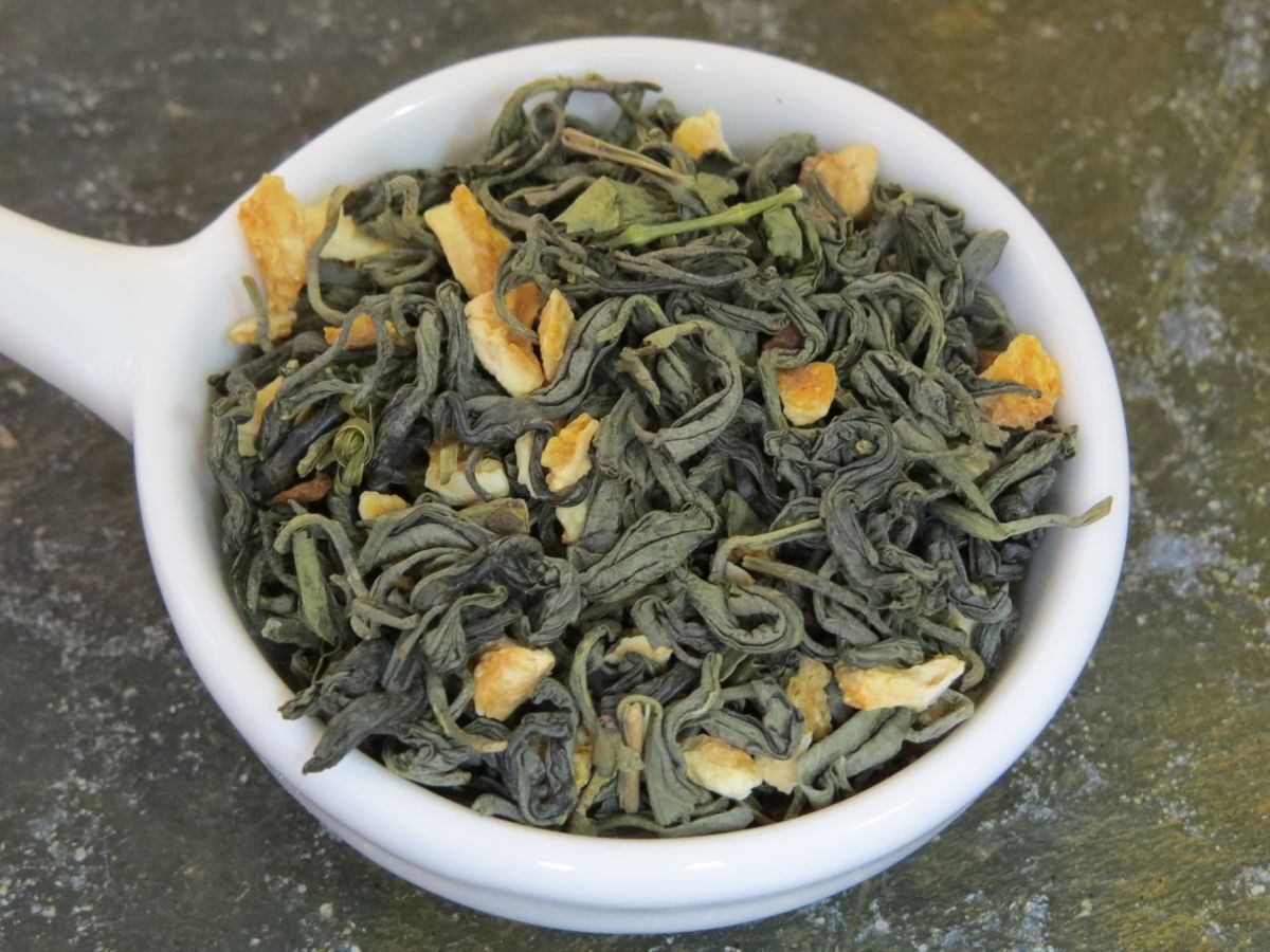 A small white bowl with a handle full of a blend of green tea, lemon peel, and cinnamon.