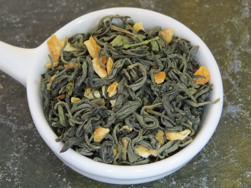 A small white bowl with a handle full of a blend of green tea, lemon peel, and cinnamon.