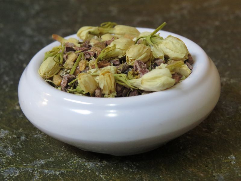 A small white bowl full of a blend of cacao nibs, jasmine flower, and spices.