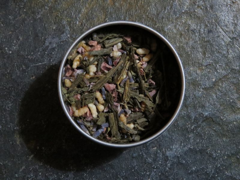 A small circular tea tin full of a blend of green tea, lavender, cacao nibs, and genmai.