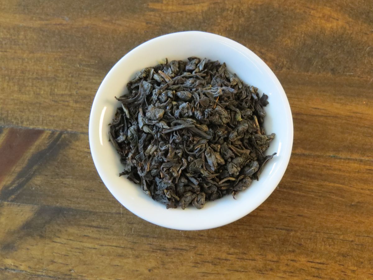 The image looks down into a small white bowl full of a blend of green and black tea.