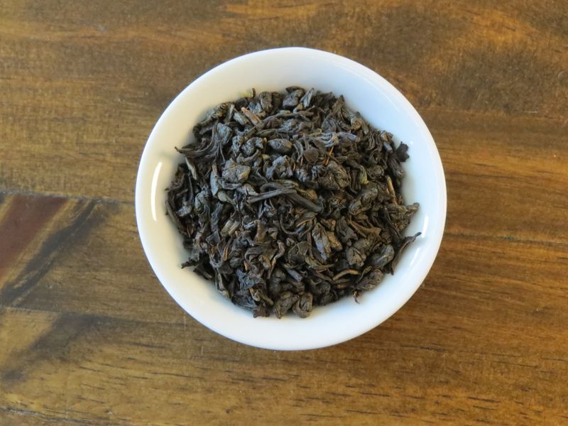 The image looks down into a small white bowl full of a blend of green and black tea.