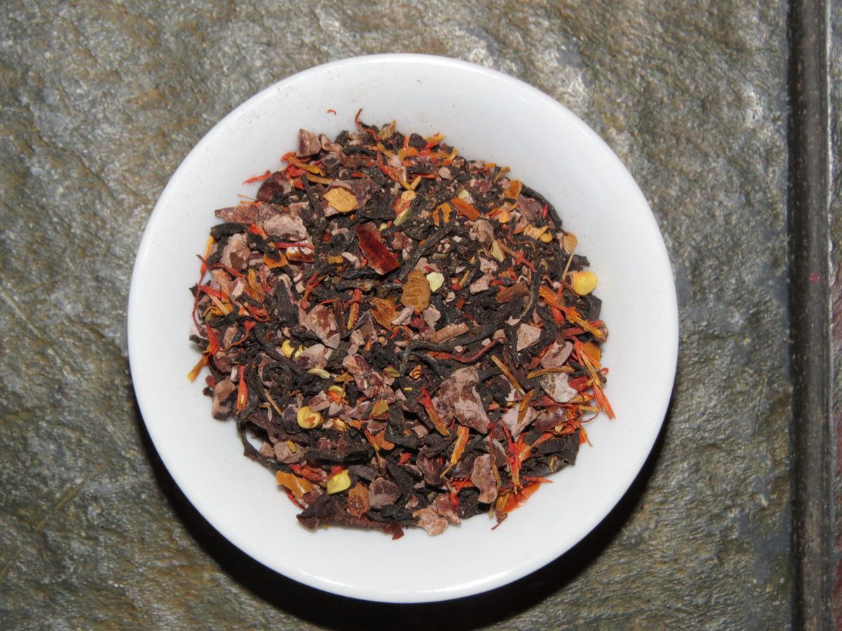 The image looks down into a small white bowl full of a blend of cacao nibs, black tea, red chile, and safflower.