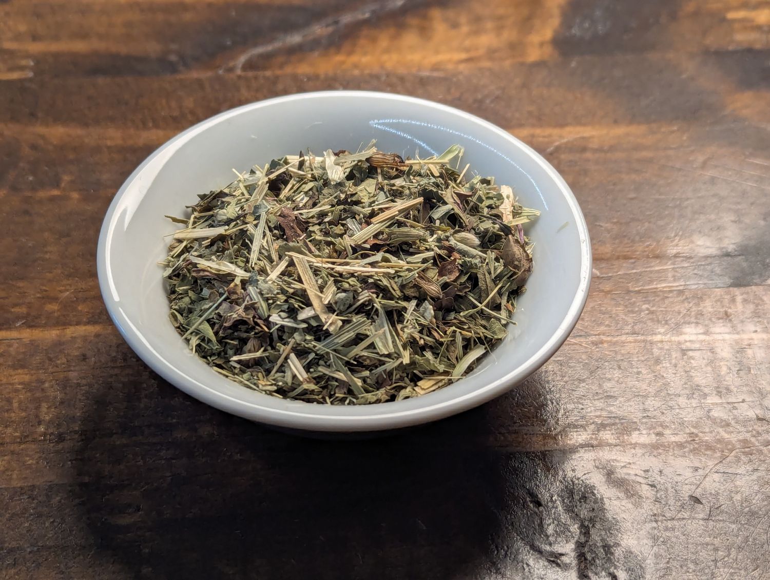 A small white bowl full of a blend of catnip, peppermint, and oatstraw.