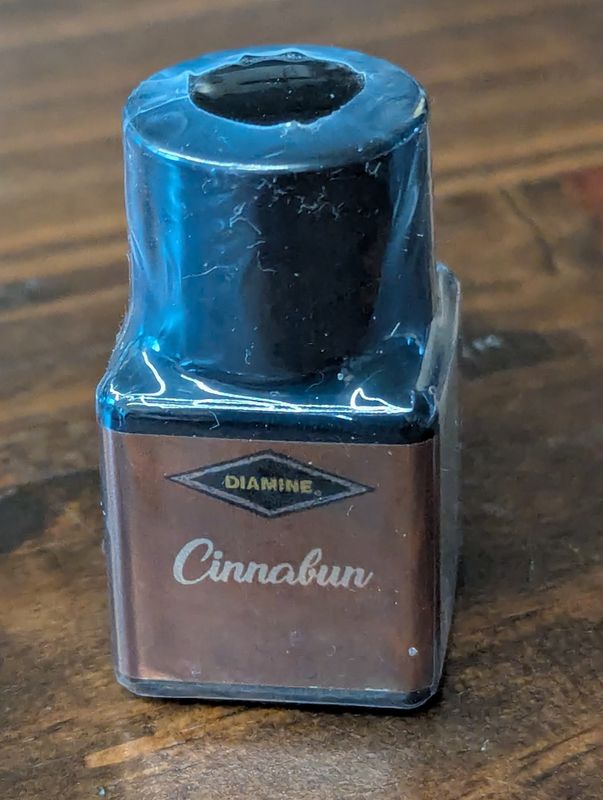 A plastic bottle with a black lid labeled "Diamine Cinnabun," still heat-sealed.