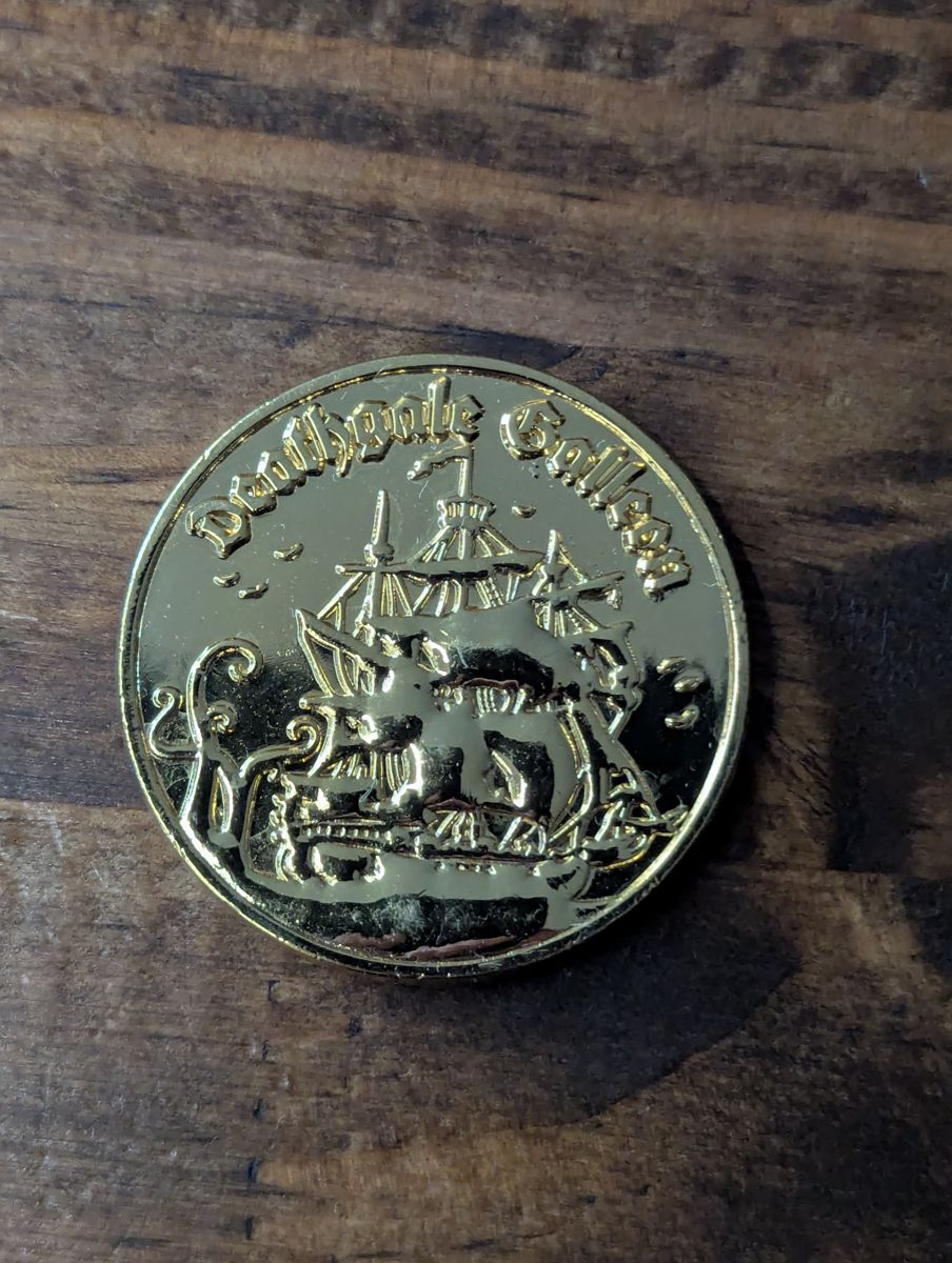 A goldtone coin showing a ship surrounded by tentacles with the words Deathgale Galleon above the image.