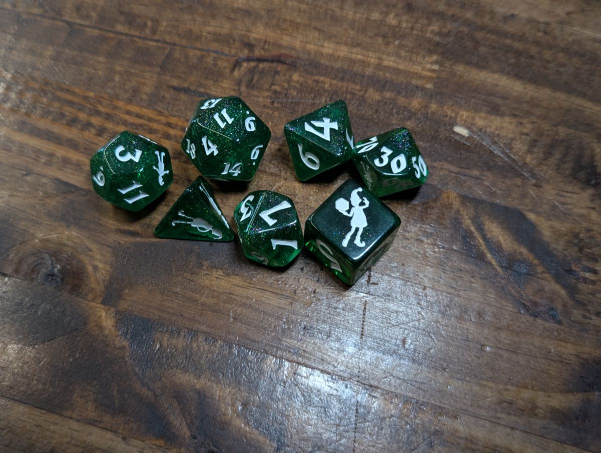 A set of green dice with glitter inside, numbers done in white, with a holiday elf replacing the highest.