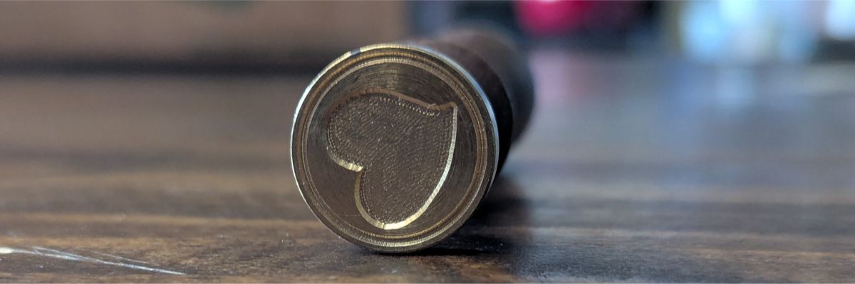 A wooden handled wax seal stamp turned so that you can see the bottom part that stamps a heart.