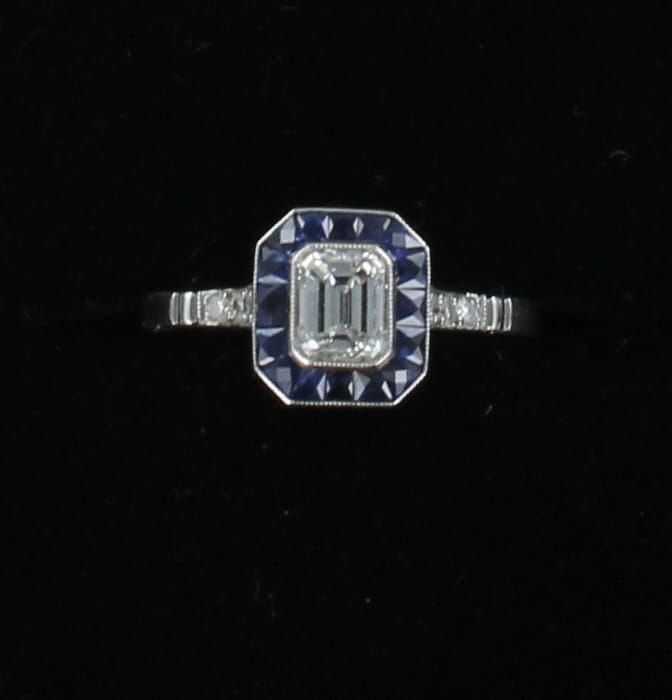 PLATINUM .71 CT EMERALD CUT DIAMOND SURROUNDED BY SAPPHIRES ENGAGEMENT RING CIRCA 1920