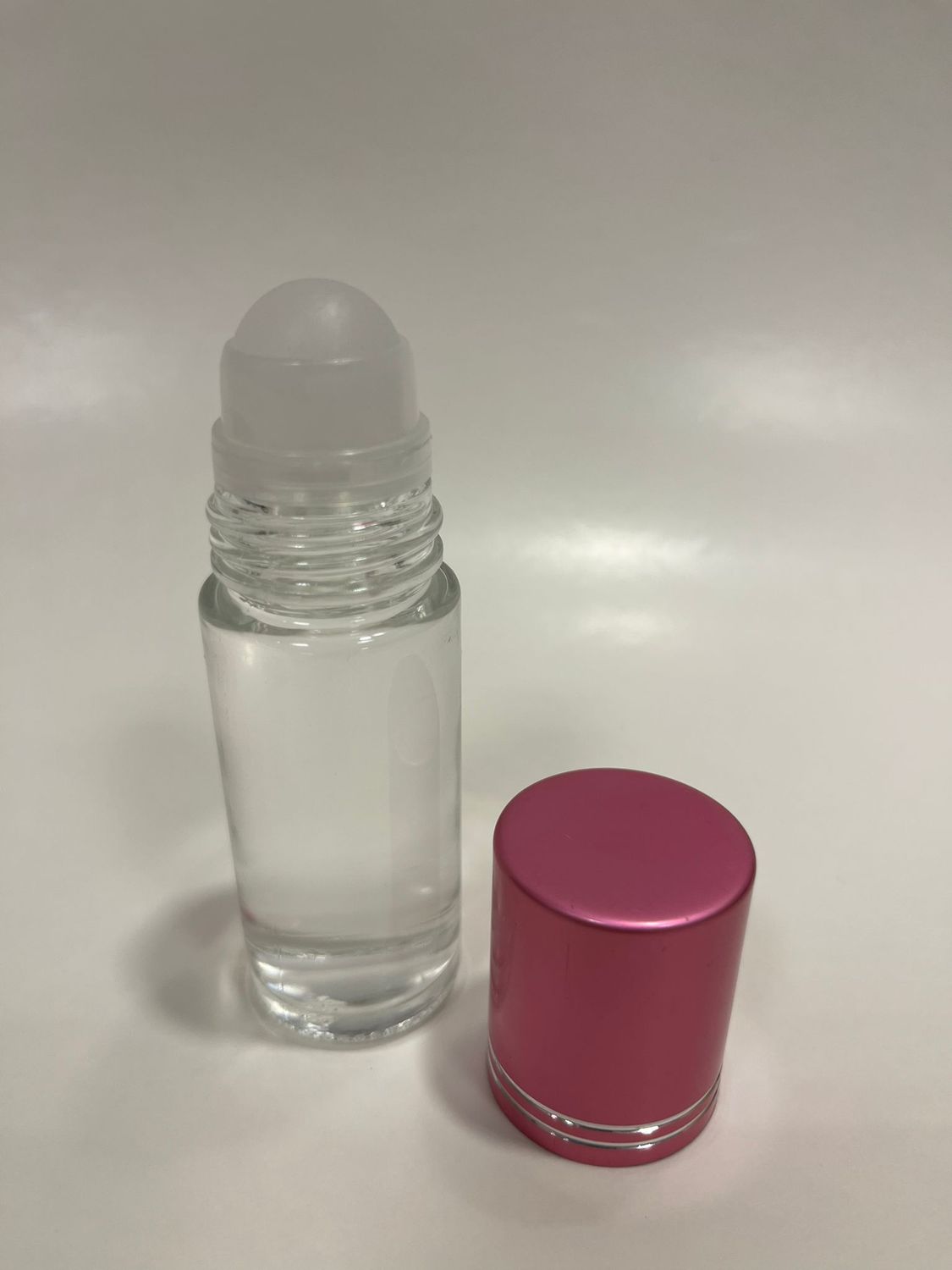 Picture of a clear glass roll-on bottle and a shiny pink cap.