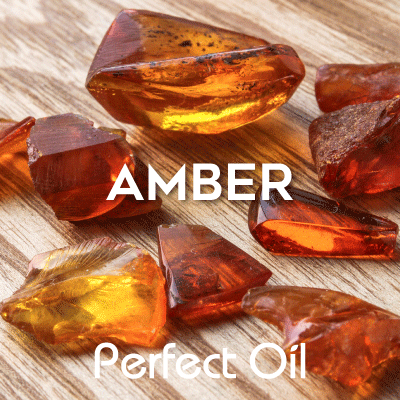 Picture showing amber stones on a wooden table with the words amber and Perfect Oil in white on top of the picture. 
