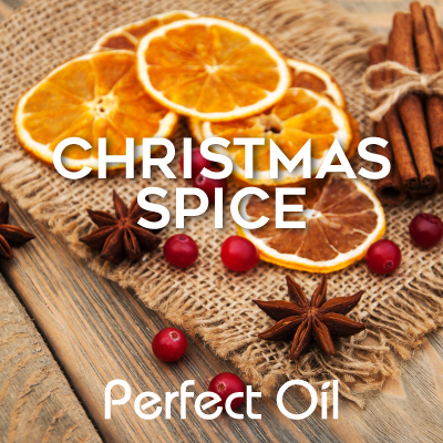 Picture of six orange slices with six holly berries and two wooden star-shaped decorations next to a small stack of cinnamon sticks banded together by rope with a knot, atop a woven placemat on a wood-slatted table with the words Christmas spice and Perfect Oil in white on top of the image. 
