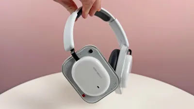 Nothing headphones, white and gray color, overhead style, held by hand, on white table against pink background.
