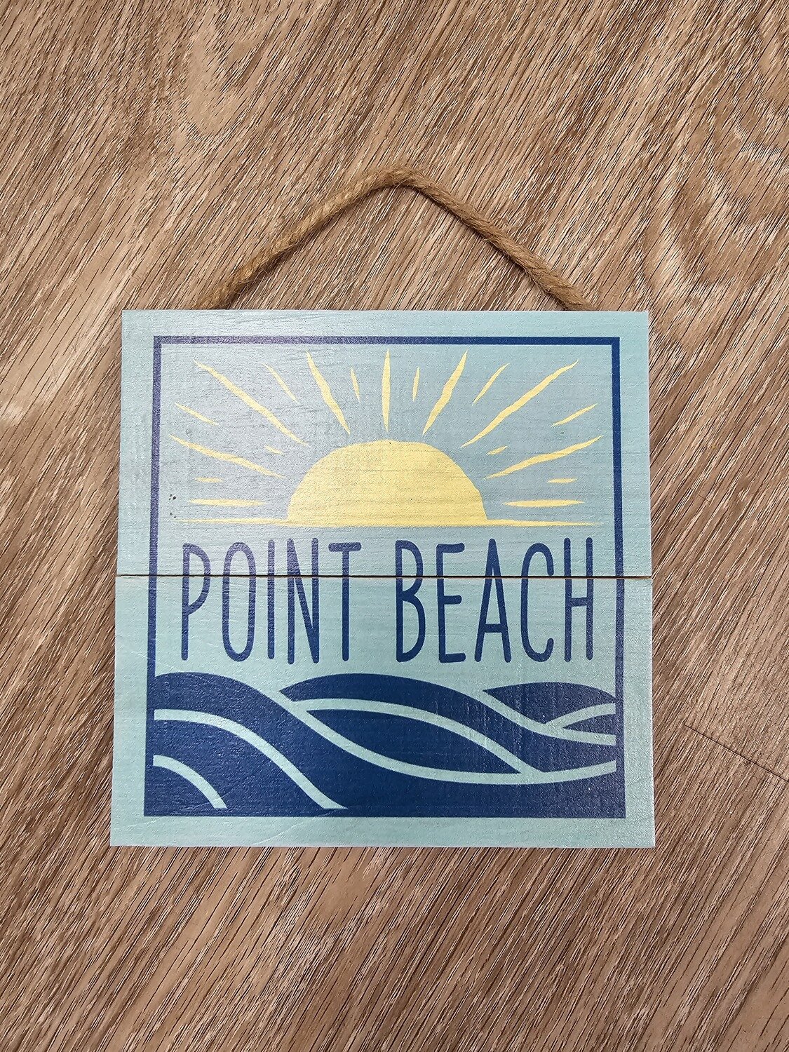A light blue square wooden hanging sign with a yellow sun above the words Point Beach and dark blue waves below