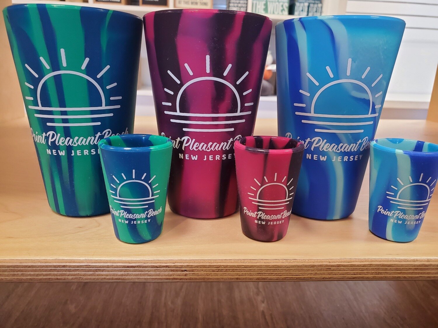 Four silicone shot glasses shown with four similar Pint glasses with white sun designs that say Point Pleasant Beach 