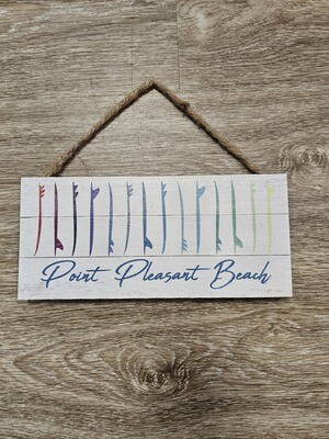 A rectangular wood sign with a drawings of surfboards lined up vertically and organized in a rainbow of colors with the words Point Pleasant Beach on the bottom