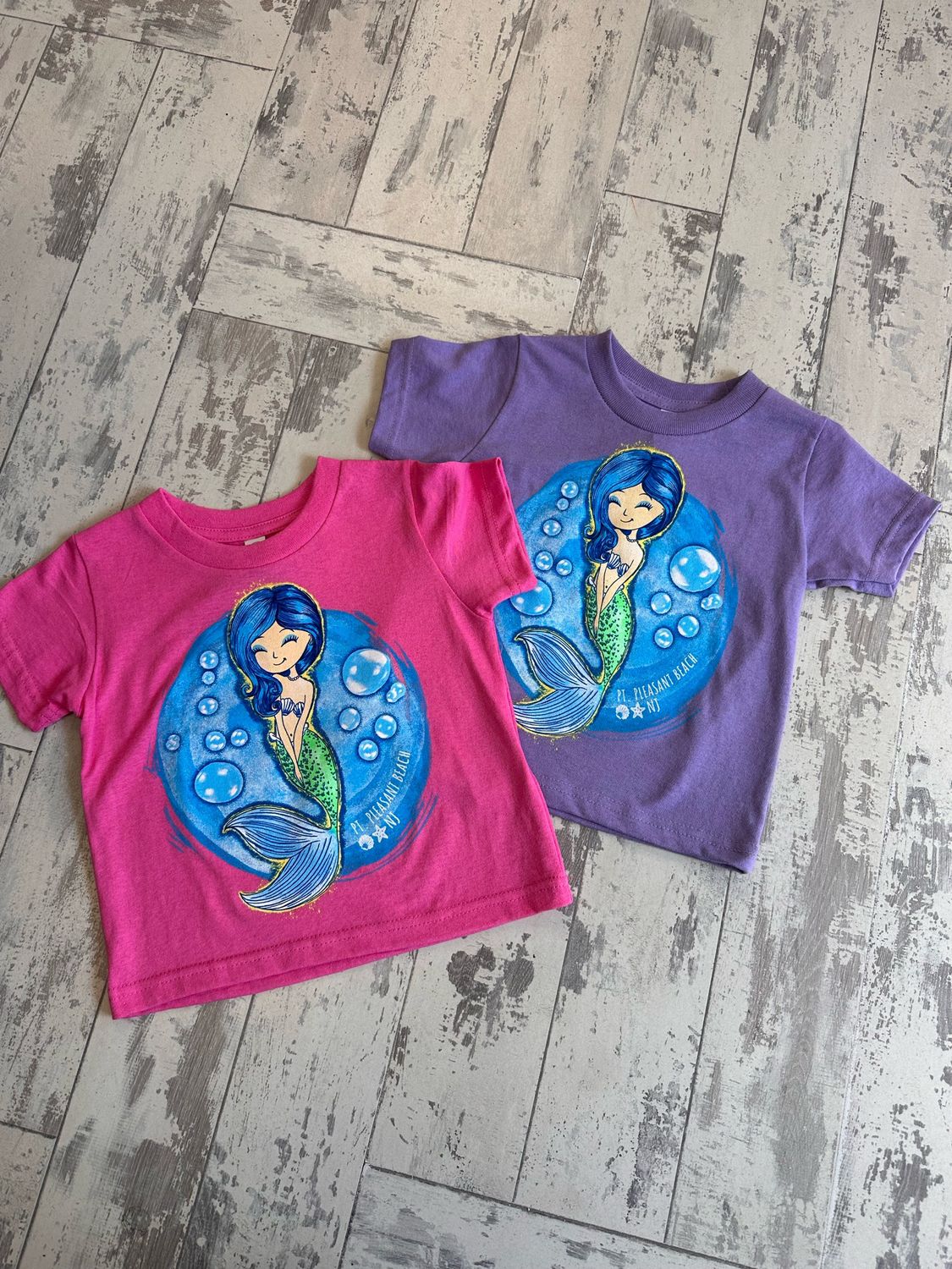Toddler T-shirts in raspberry pink and lavender purple featuring a playful mermaid design surrounded by bubbles and &quot;Pt. Pleasant Beach, NJ&quot; text.