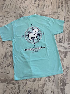A light aqua t-shirt showcasing a navy graphic of a compass with a cartoon dog in the center, accompanied by the text &quot;Jenkinson&#39;s Boardwalk, Point Pleasant Beach, NJ&quot; below.