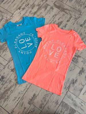 Two junior t-shirts in sky blue and coral colors with a &quot;LOVE&quot; design encircled by the text &quot;Point Pleasant Beach, NJ,&quot; displayed on a rustic wooden floor
