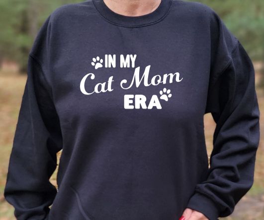 In my Cat Mom Era Unisex Tshirt or crewneck sweatshirt with option for providing for pawsLogo on back