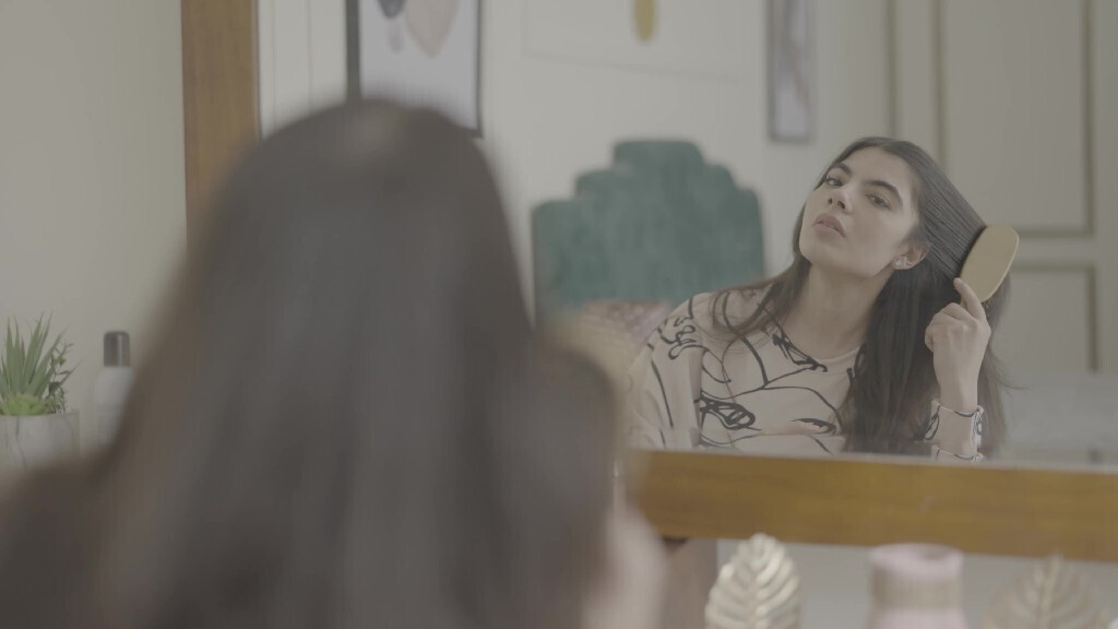 a woman sitting in front of the mirror brushing her hair