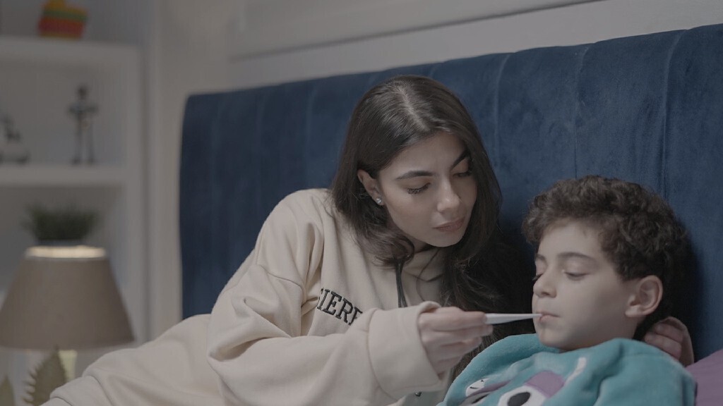 a woman sitting in bed takes her son&#39;s temperature